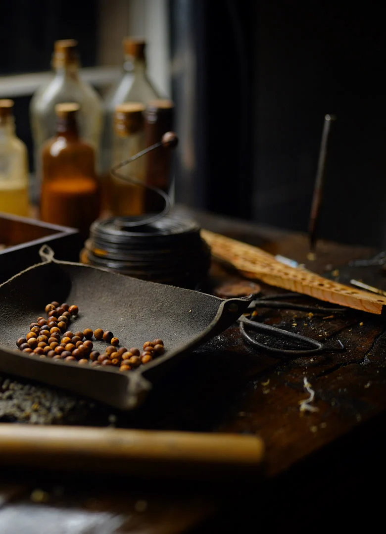 The Cypress Pebble bench: trays of cypress beads, corked bottles, a steel rule and a hammer under window light
