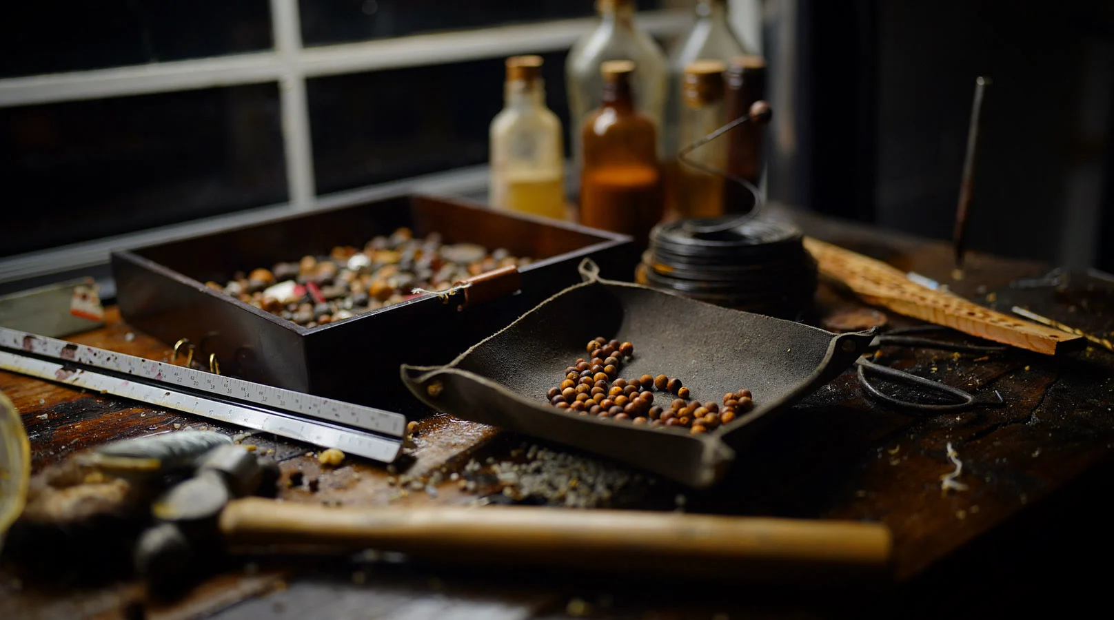 The Cypress Pebble bench: trays of cypress beads, corked bottles, a steel rule and a hammer under window light