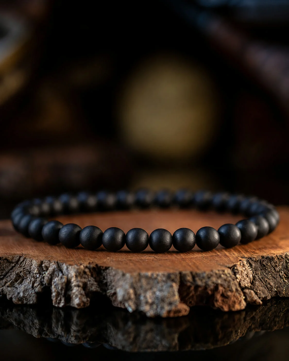 A matte black bead bracelet resting on a slice of cypress