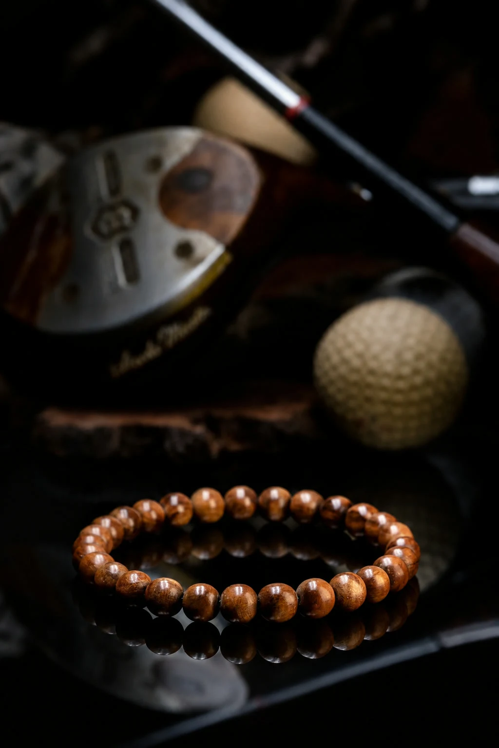 A cypress bead bracelet on black glass, an antique golf ball and hickory club heads softly behind