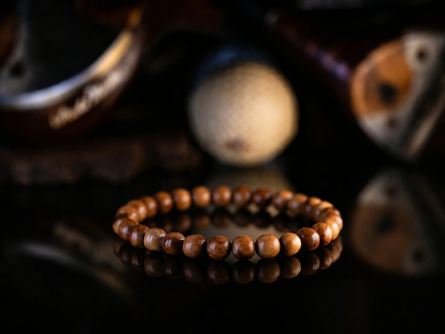 A cypress bead bracelet on black glass, an antique golf ball and hickory club heads softly behind