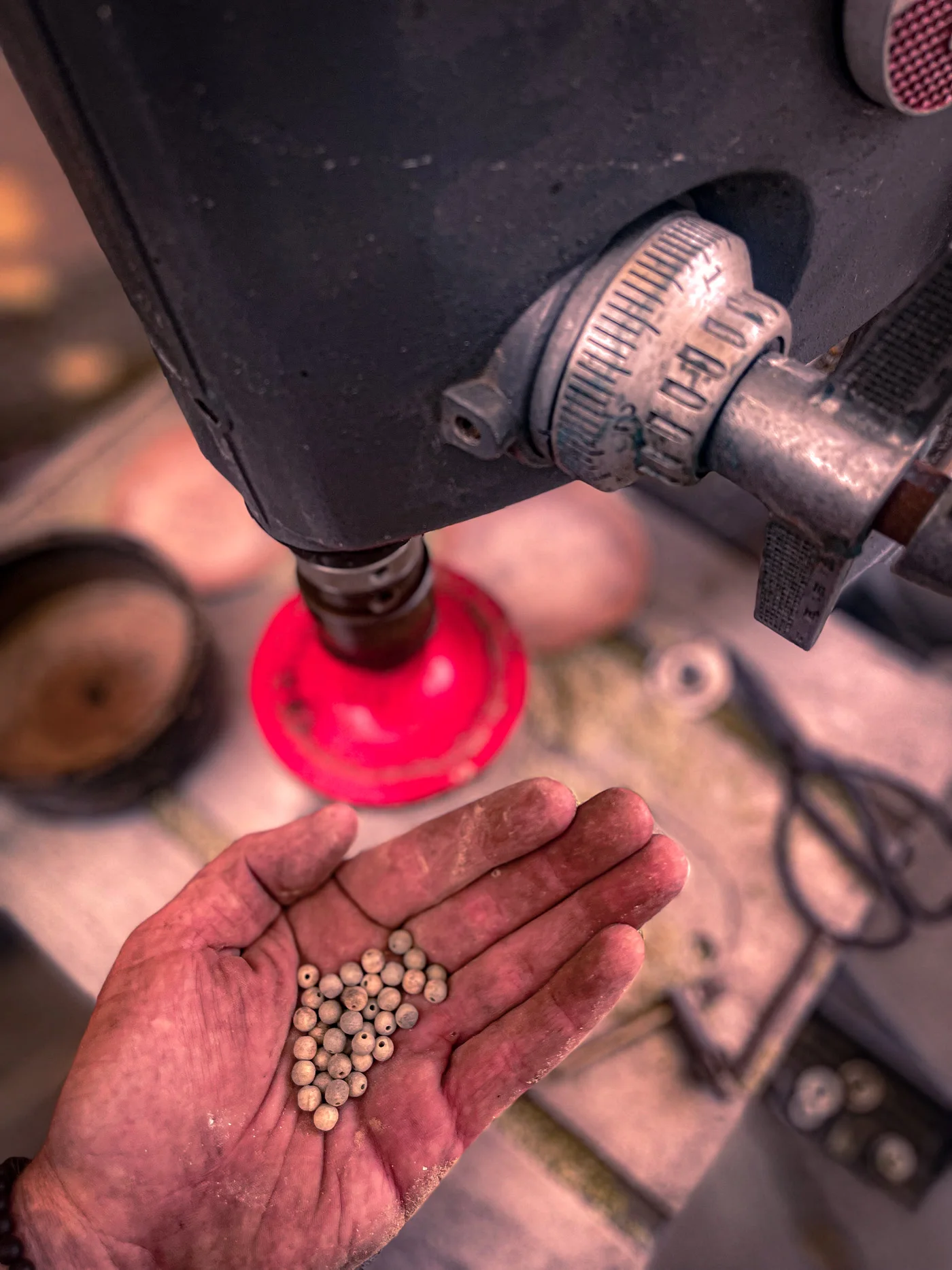 An open hand holding drilled beads beneath a drill press
