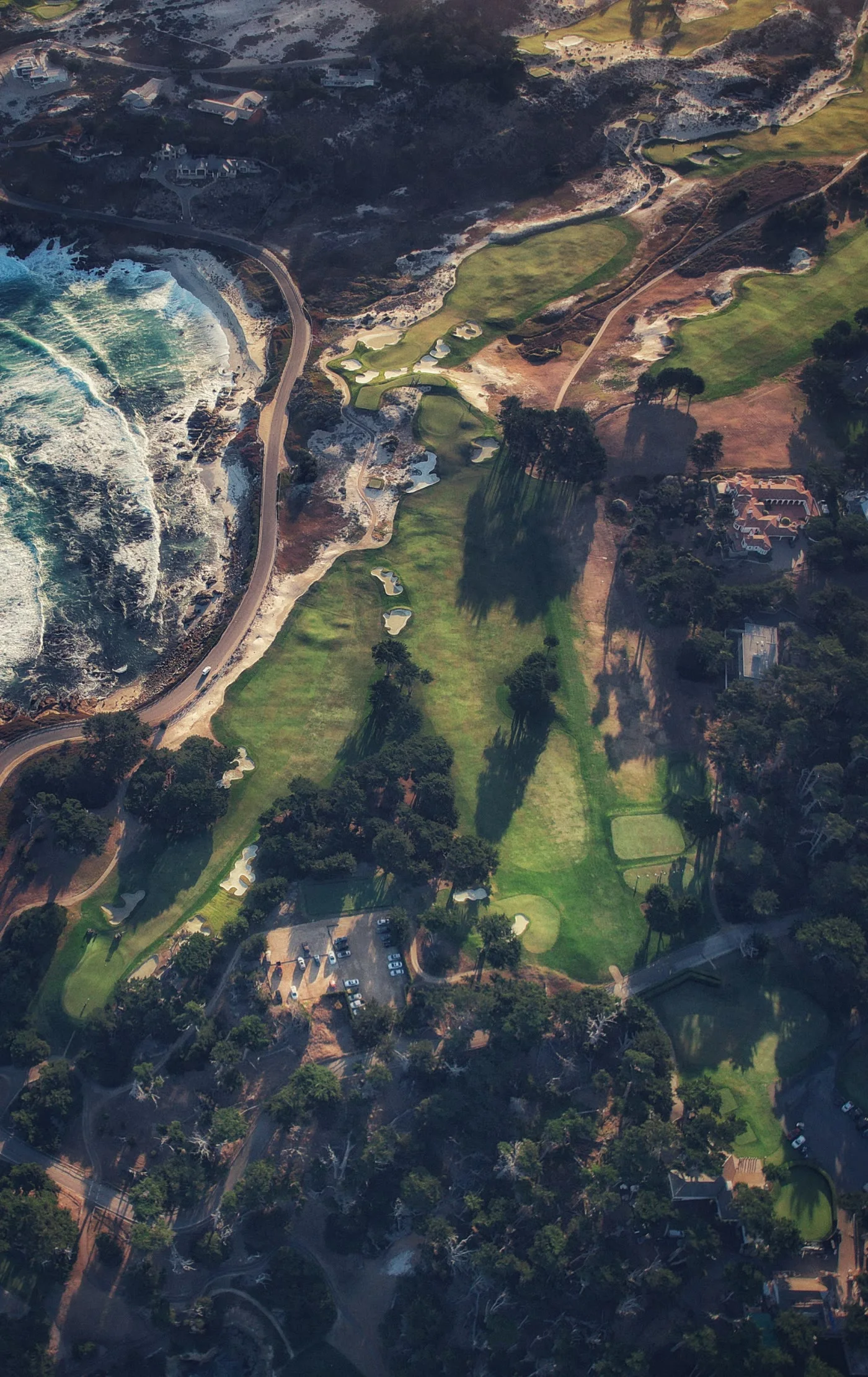 Aerial of the Monterey coast: surf breaking along the shore road, fairways running through the dunes